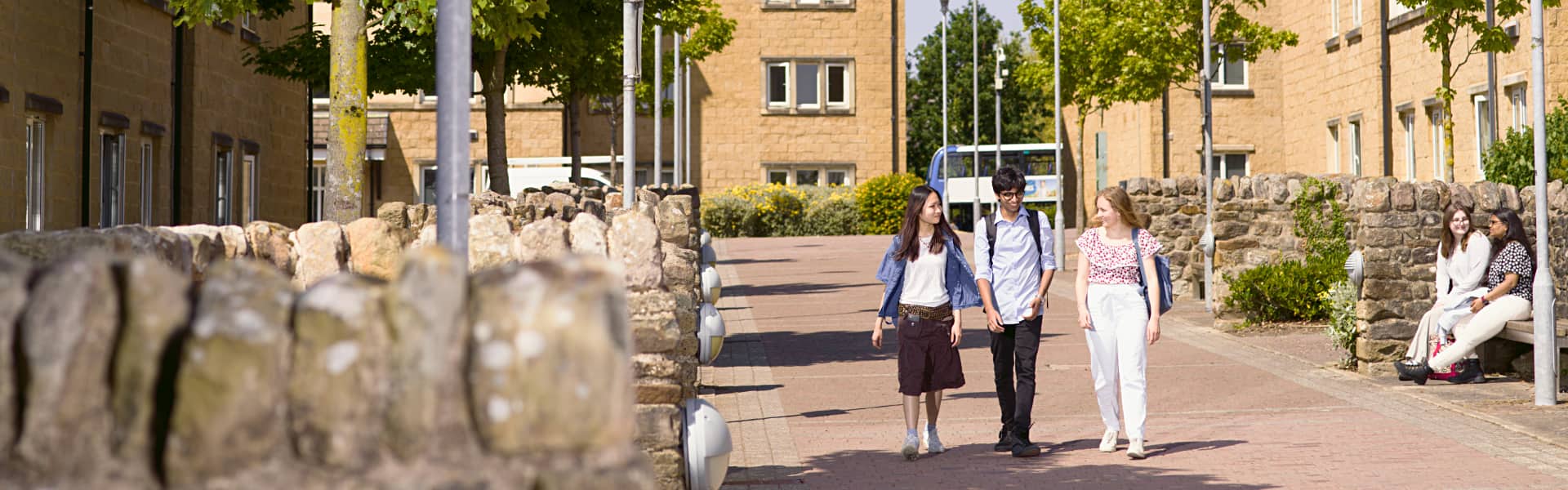 Students walk between a series of accommodation blocks, surrounded by trees and dry stone walls.