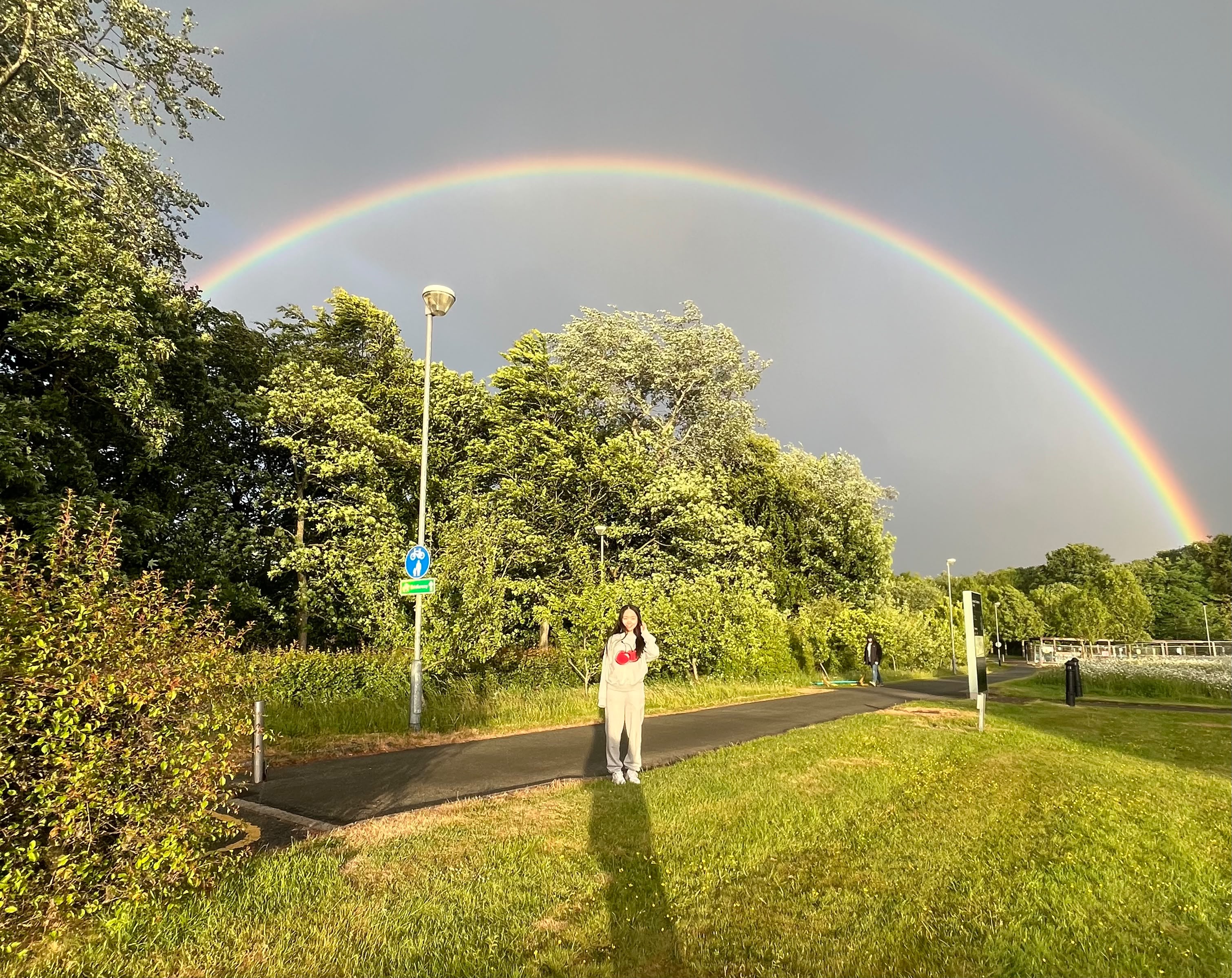 A person on the pavement with a rainbow above her head.