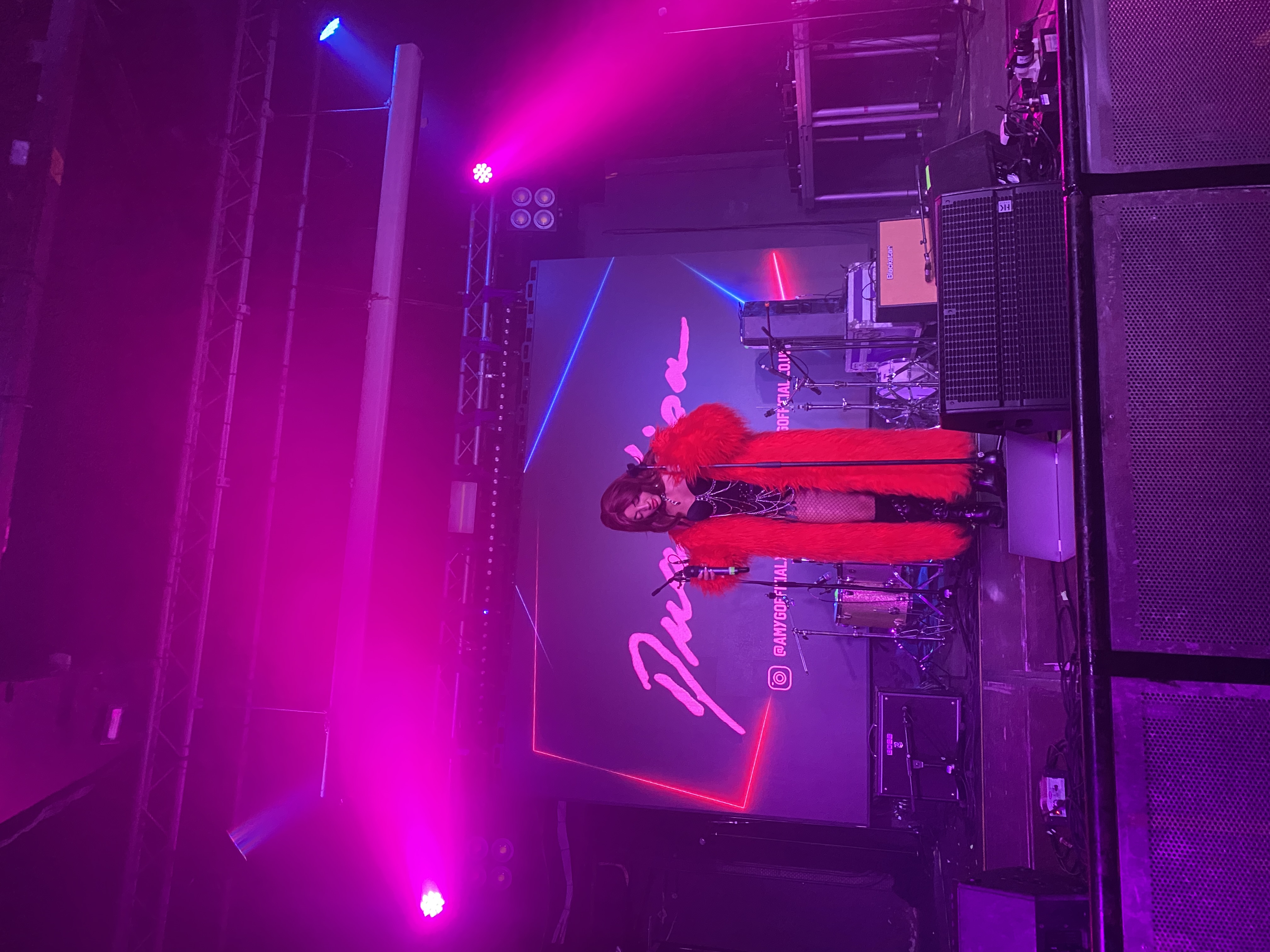 A person stands at the microphone, ready to sing on a stage bathed in purple and pink light.