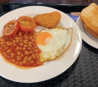 A plate with tomatoes, fried egg, baked beans, hash brown, and white toasts.