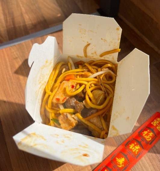 A box of hot chilli noodles with chopsticks on the side.