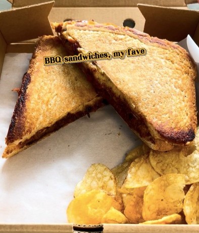 A BBQ pork sandwich in a box with crisps.