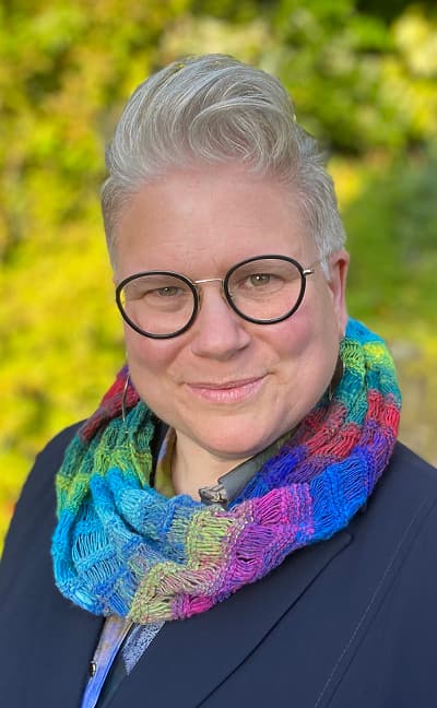 Claire stands outside wearing a colourful scarf and glasses.