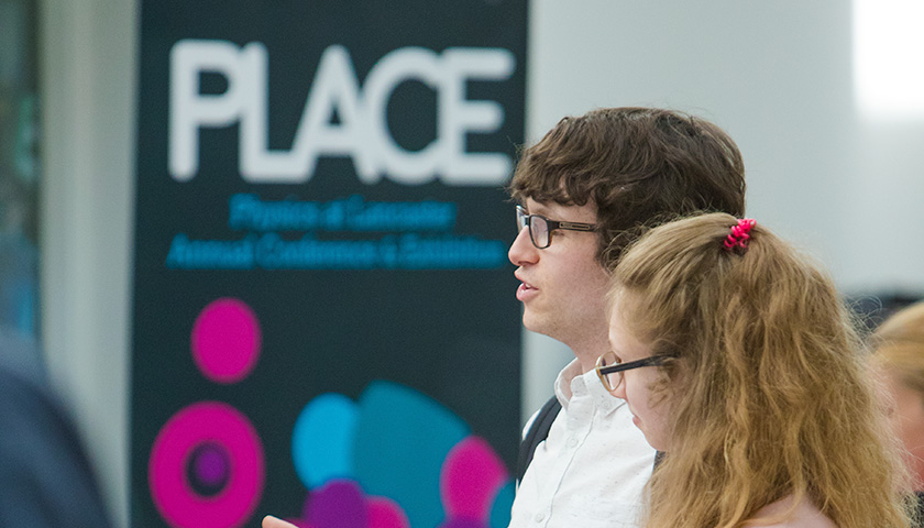 Two students stood talking in front of a banner reading The PLACE