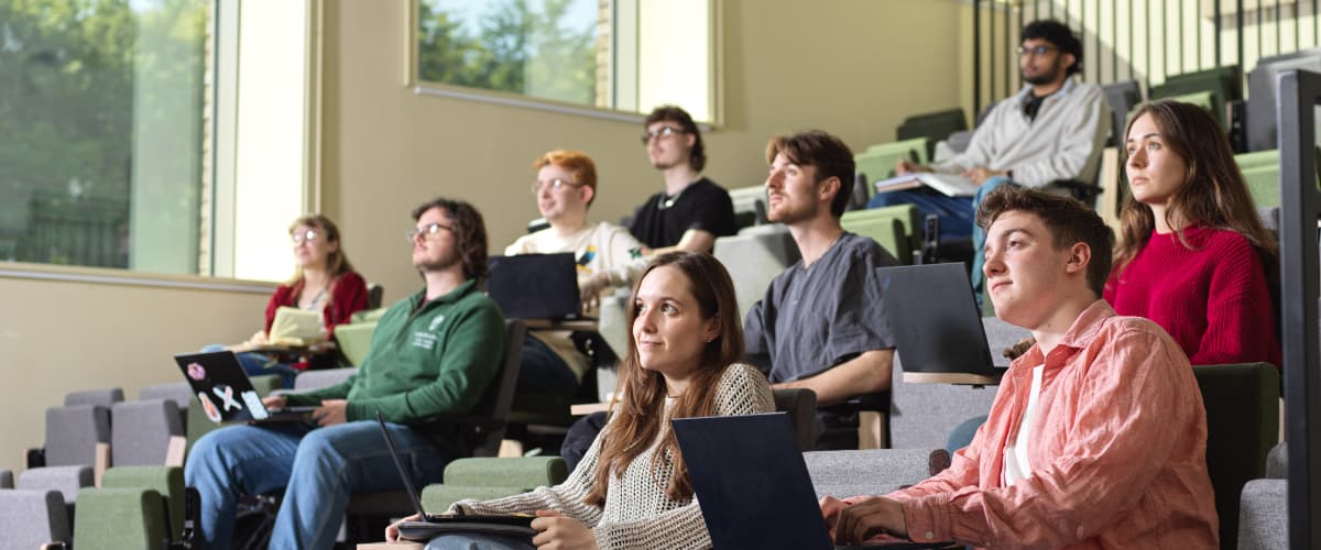 Students sit in rows in a lecture theatre and pay attention.