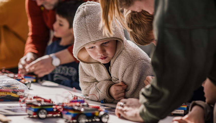 a child in a grey hoodie looks at some lego vehicles
