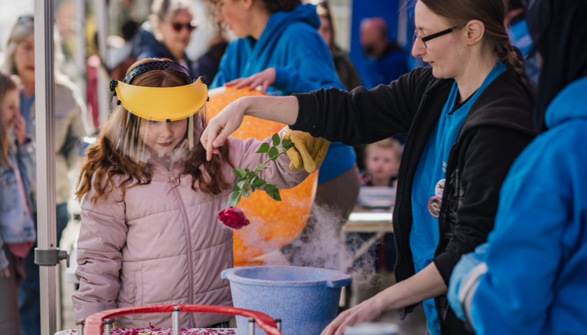 a child wears a visor and hold a red rose about a blue tub with smoke coming out of it