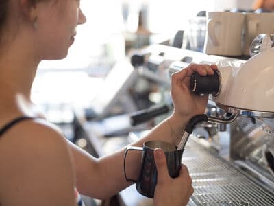 A barista operating an espresso machine, steaming some milk for a coffee.