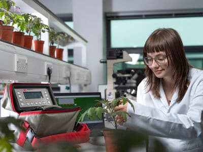 A person in a laboratory coat examines a plant at a lab bench beside scientific equipment.