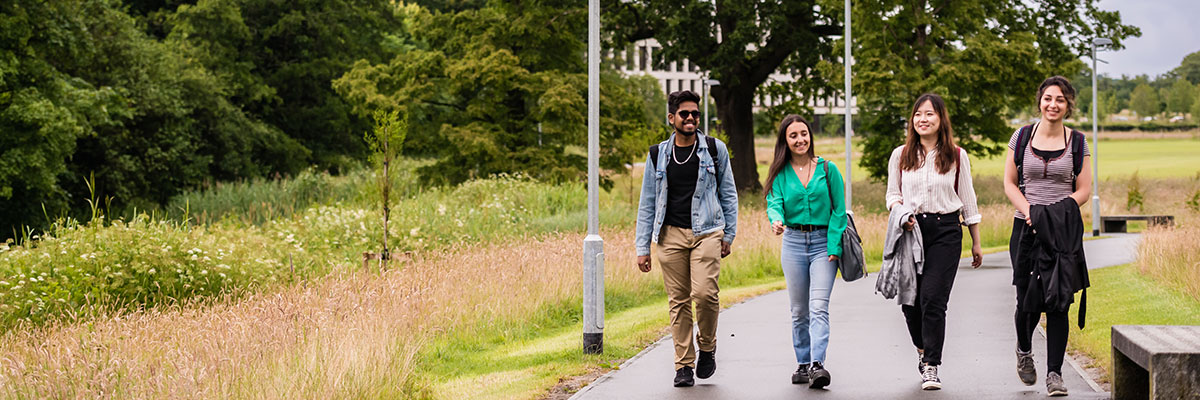 A diverse group of students walking in the lush grounds of the University, smiling and chatting.